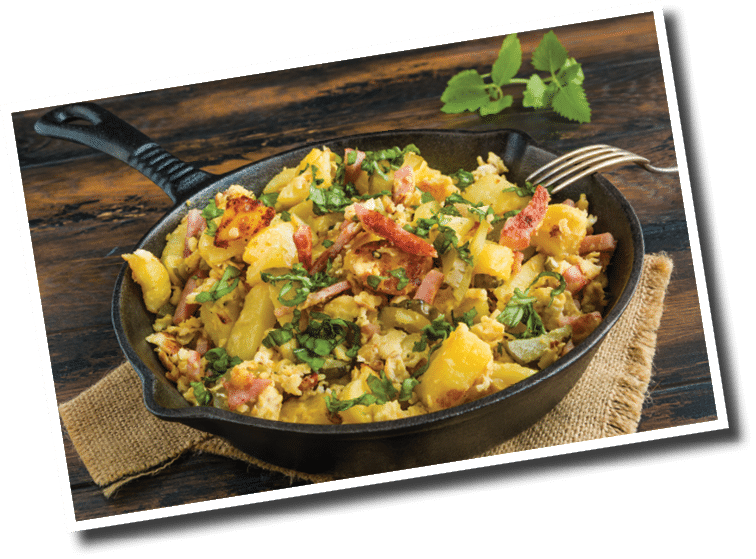 Traditional German dish Hoppel Poppel - fried potatoes, eggs, marinated cucumbers. Black cast-iron skillet on wooden table.